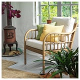 Cozy indoor seating area with a wicker chair, yellow and green cushions, a small wood stove, and plants.