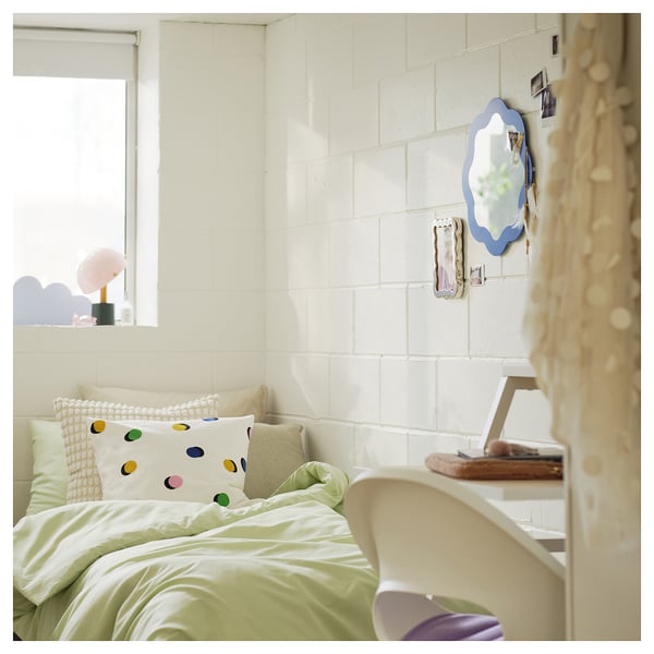Bedroom with white bed, colorful pillows, laptop on chair, and wall mirror with blue frame.