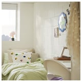 Bedroom with white bed, colorful pillows, laptop on chair, and wall mirror with blue frame.