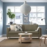 Modern living room with PÄRUP olive sofa, natural wood coffee table, and a large window. Cozy & minimalist decor.