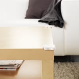 A corner of a wooden table with a white safety bumper attached to protect from injuries.