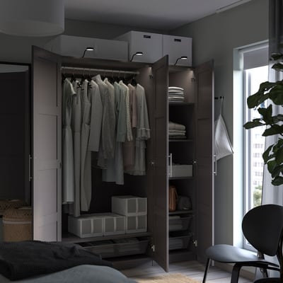 An open dark brown PAX wardrobe with clothes and organizer boxes.