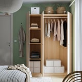 Wooden wardrobe with shelves and hangers, organizing clothes and bedding near a bed.