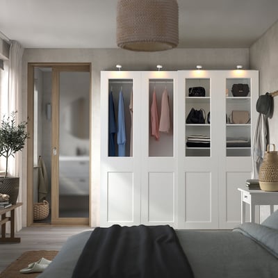 Modern bedroom with large white PAX wardrobe, showing clothes and folded items. Wardrobe towers over bed with grey blanket.