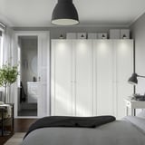Minimalist bedroom with white PAX wardrobe, gray bed, wooden floor, and hanging plant.