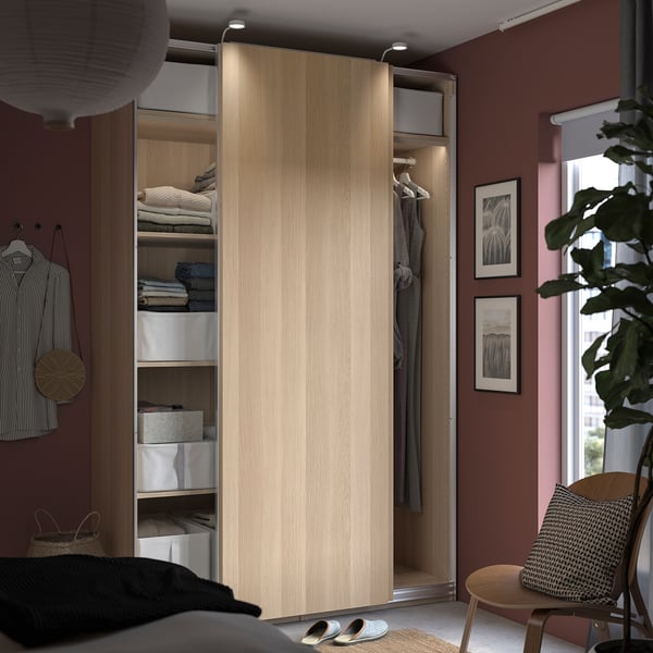 Modern bedroom with PAX wardrobe, built-in lights, organized clothes, striped wall, small table, and plant.
