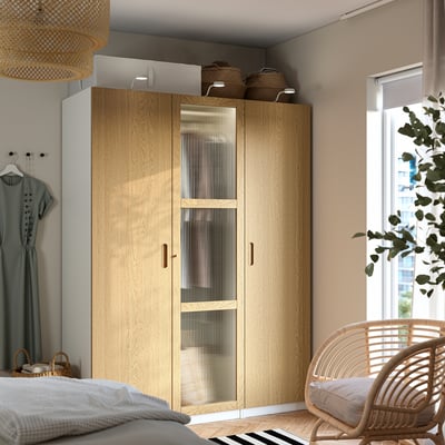 PAX wardrobe in bedroom with glass door, baskets, wicker chair, natural light.