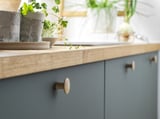 Modern kitchen counter with gray cabinets, light wood countertop, and plants. Round wooden knobs on drawers.