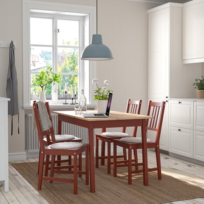 Small, red, wooden dining set with cushioned chairs, centered under a large light, next to kitchen cabinets.