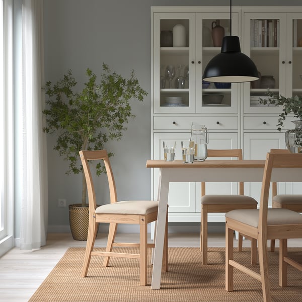 Minimalist dining setup with wooden table, chairs, pendant lamp, plant, and cabinet.