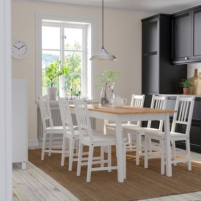 Cozy kitchen with white PINNTORP dining set. Six matching chairs, brown rug, dark cabinets, hanging light.
