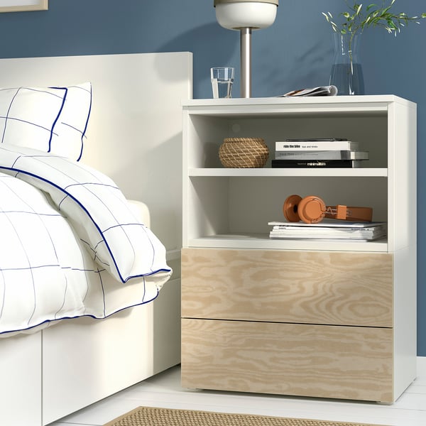 Modern bedroom with white nightstand, books, lamp, plant, blue-trimmed bed. Or bedroom: white nightstand with books, lamp, plant, blue-trimmed bed.