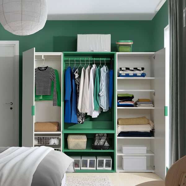 Modern bedroom closet with green PLATSA units, hanging shirts, folded sweaters, boxes, and a light fixture.
