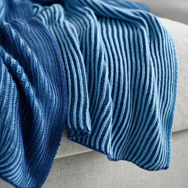 Thick, knitted blue blanket with ribbed pattern, draped cozily on a bed or sofa.