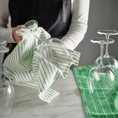 Person dries clear glasses with green-striped RINNIG tea towel, showcasing kitchen cleaning aid.