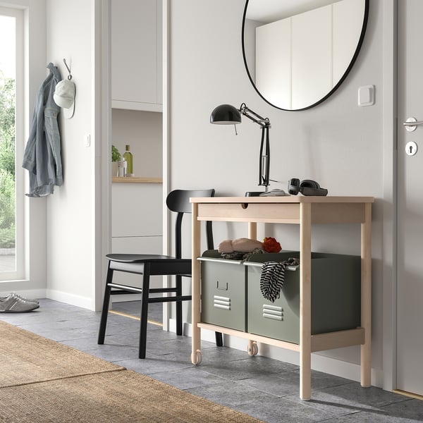 Modern entryway with light wood trolley, green bins, mirror, lamp, and black stool.