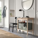 Modern entryway with light wood trolley, green bins, mirror, lamp, and black stool.