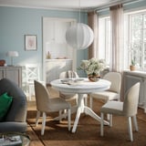 Light blue dining room with white extendable table, beige chairs on jute rug, and pendant light.