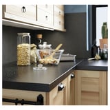 Modern kitchen counter with wooden cabinets, black speckled top, pasta, utensils, plant, under-cabinet lights.