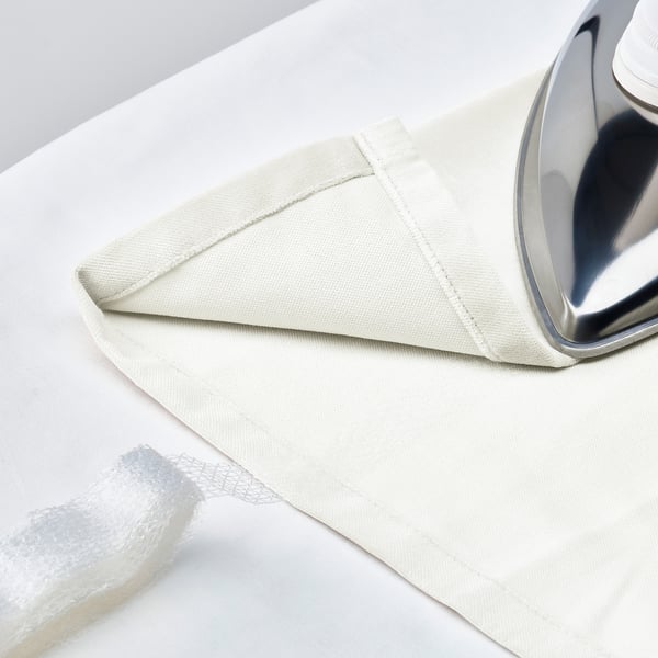 A silver iron rests on off-white SANELA curtains laid out flat, ready for pressing.
