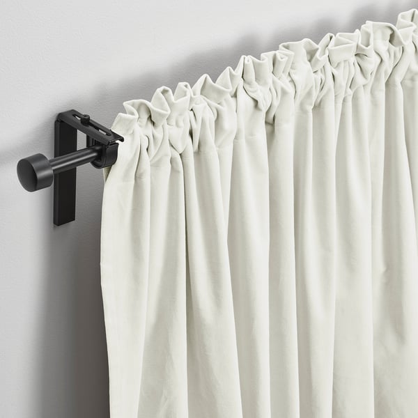Off-white velvet curtains hang elegantly, filtering light softly. Matte black rod and brackets provide a sleek, modern contrast.