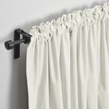 Off-white velvet curtains hang elegantly, filtering light softly. Matte black rod and brackets provide a sleek, modern contrast.