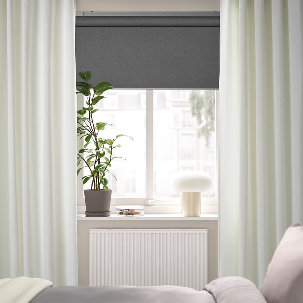 Minimalist bedroom window with off-white curtains, plant, lamp, and radiator.