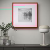 Red-framed nature photo on black cabinet, flanked by vases with leaves and a white lamp.