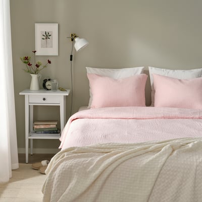Light pink SCHERSMIN duvet set on bed, with nightstand, lamp, flowers, clock, books.