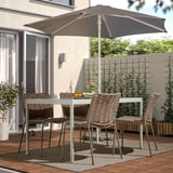 Modern outdoor patio with rectangular table, four wicker chairs, large grey umbrella. Cozy setup with wooden deck, house in background.