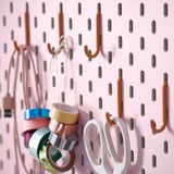 Pegboard with orange hooks holding colorful tapes and white scissors, organized for crafting or office use.