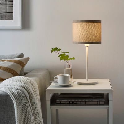 Cozy living room with SKAFTET lamp on side table, next to sofa with blanket and books.