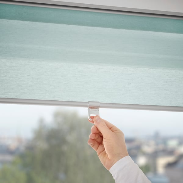 Hand adjusts cordless roller blind, ensuring safe, soft closure, filtering daylight.