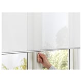 Hand pulls white roller blind downward, showing soft light filtering and cordless design for safety.