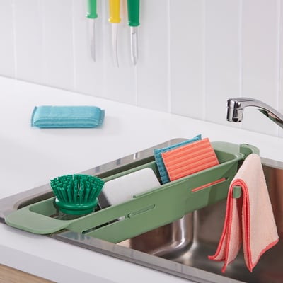 Green sink organizer with brush, soap, and towels for efficient cleaning.