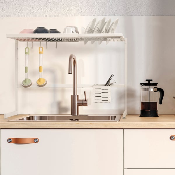 Kitchen sink with white dish drainer holding dishes and cutlery, freeing counter space and adjusting size.