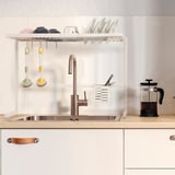 Kitchen sink with white dish drainer holding dishes and cutlery, freeing counter space and adjusting size.