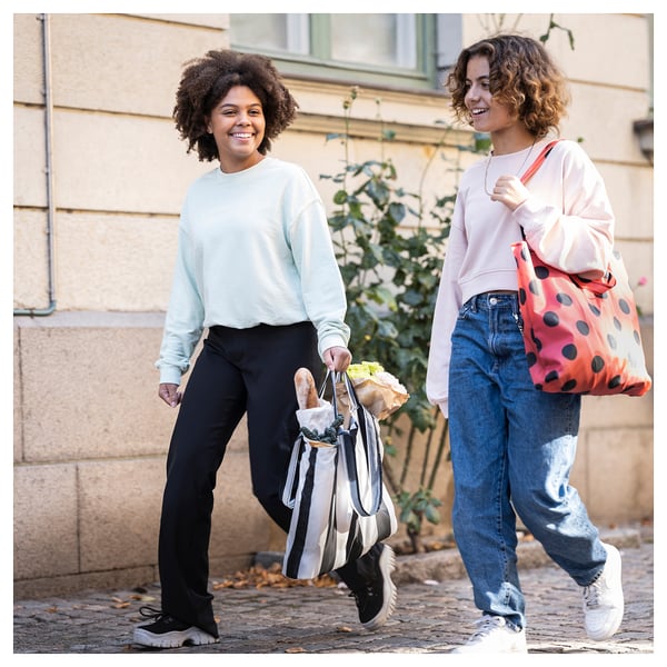 Two women smile, walking outdoors with shopping bags.