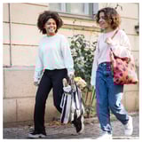 Two women smile, walking outdoors with shopping bags.