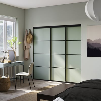 Modern bedroom with light green SKYTTA wardrobe featuring frosted glass doors, a white chair, and a huge window allowing ample sunlight.