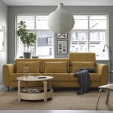 Modern living room with mustard sofa, round table, rug, and large windows.