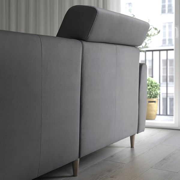 A modern gray sofa with extendable back cushions for head support. The photo shows a sleek, minimalist design with wooden legs.