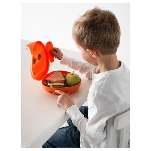 Child sitting, opening orange lunchbox with ears, containing sandwich and apple.