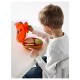 Child sitting, opening orange lunchbox with ears, containing sandwich and apple.