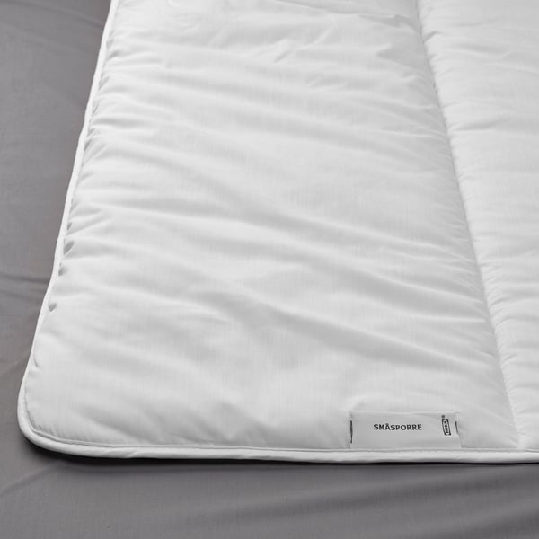 A plush, white duvet on a bed, featuring smooth fabric and a labeled tag, showcasing its soft and fluffy texture.
