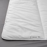 A plush, white duvet on a bed, featuring smooth fabric and a labeled tag, showcasing its soft and fluffy texture.