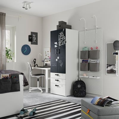 Modern teen bedroom with black and white furniture: desk, bed, wardrobe, striped rug, gray sofa, and pegboard.
