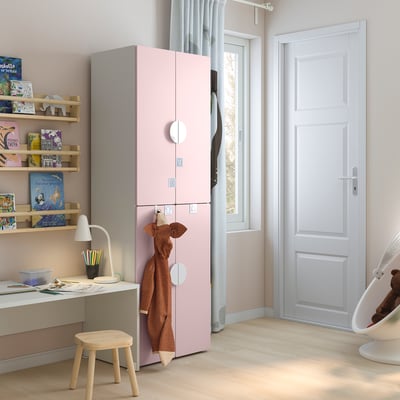 A kids room with a pink SMÅSTAD wardrobe has multiple shelves with colorful books, a desk with a lamp, and a small chair.