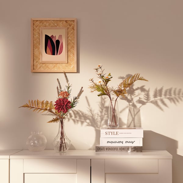 A stylish bouquet in a clear vase sits on a white cabinet, adding color and life. Above it, a woven frame picture hangs.