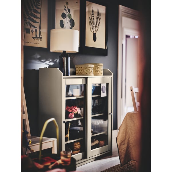 Cozy corner with lamp, glass-cabinet, wicker baskets, & nature prints.